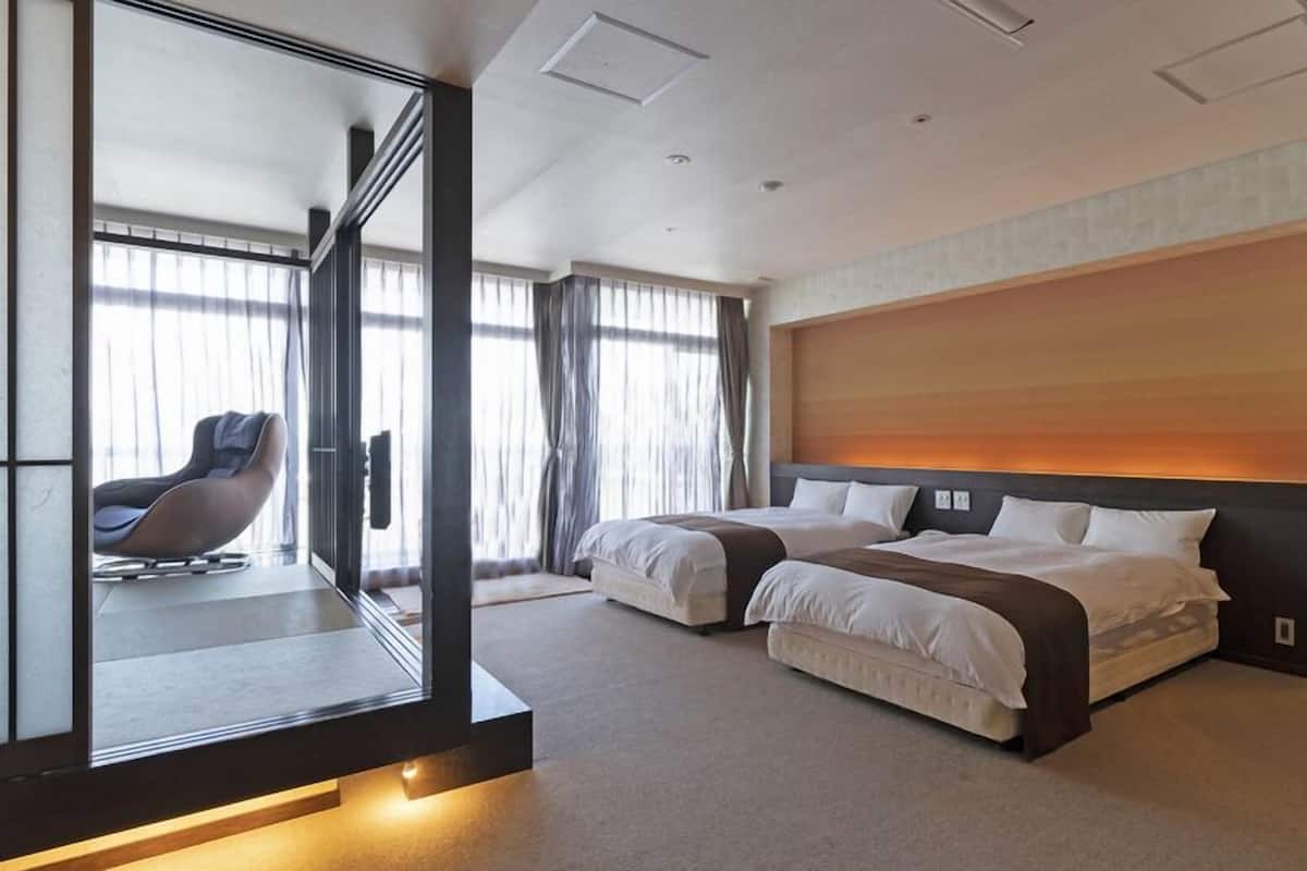 A modern hotel room with a large bed, a chair, and a view through a glass partition.