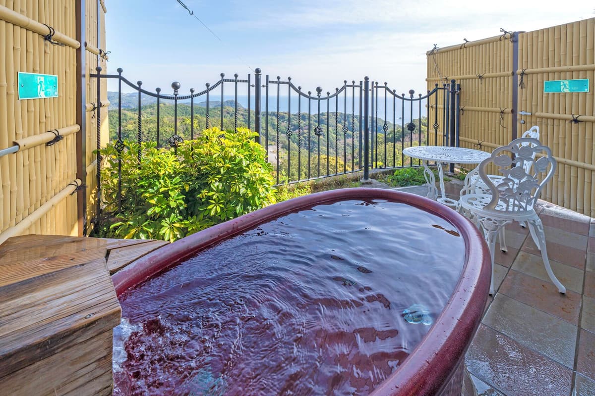 A hot tub with a wooden deck, a white table with chairs, and a bamboo fence with a view of the landscape.