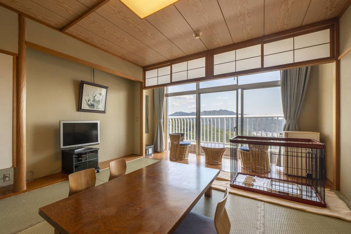 A traditional Japanese-style room with tatami flooring, a wooden table, a television, and a balcony with a view.