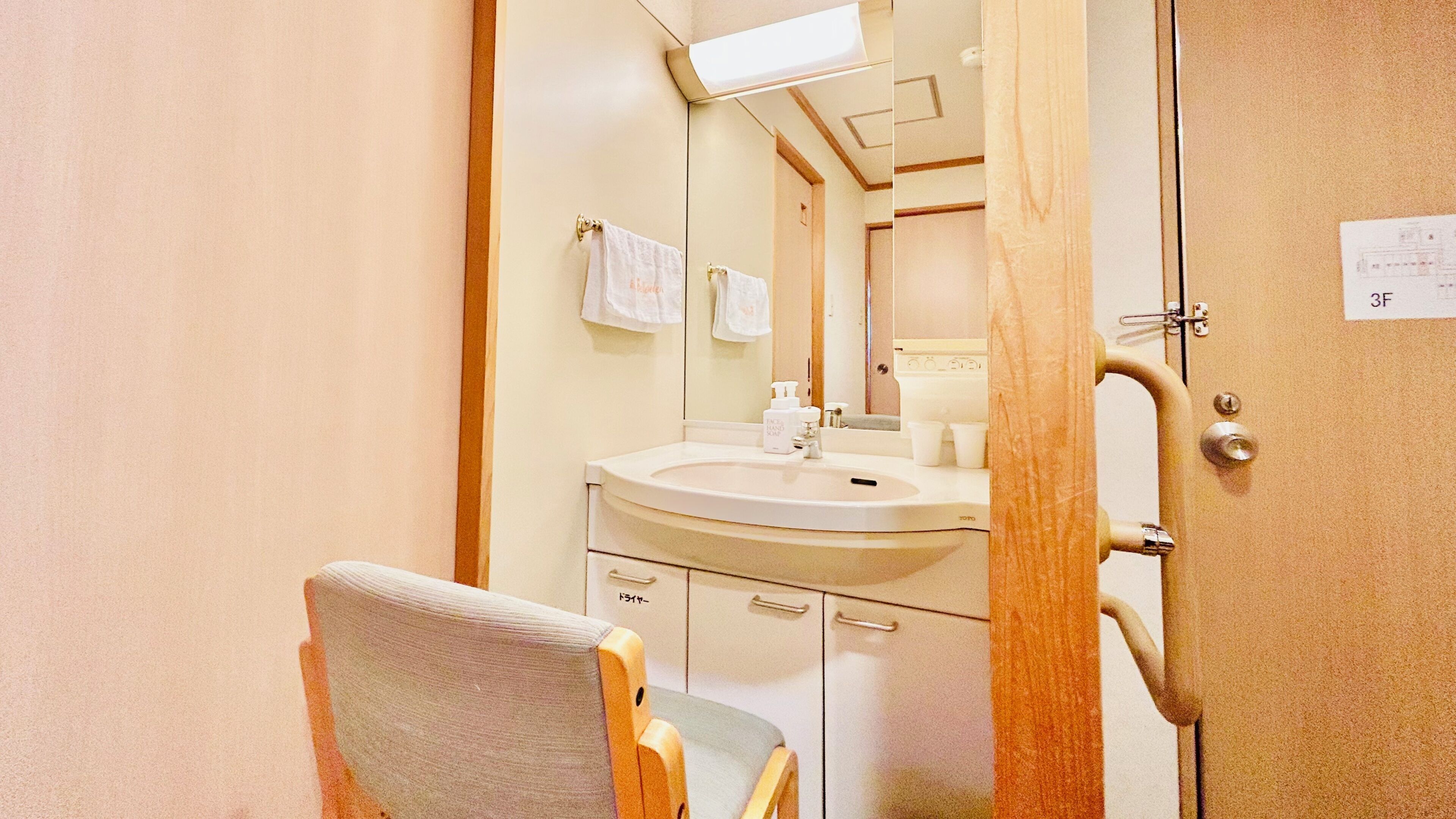 Une salle de bain équipée d’un lavabo, d’un miroir, d’un porte-serviettes et d’une chaise.