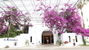 Entrada de hotel con techo de vidrio y plantas florecientes de color rosa.