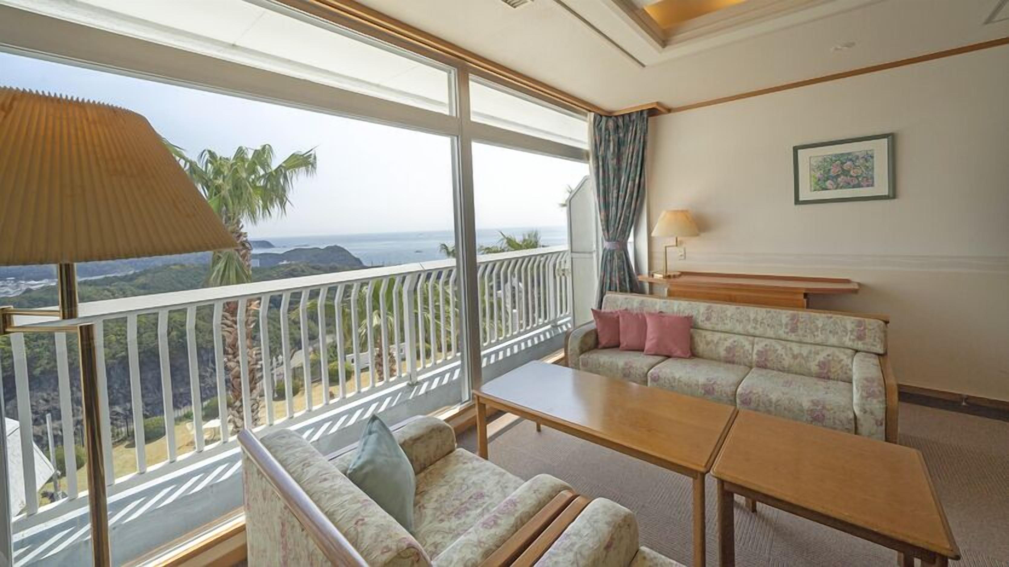 A hotel room with a balcony, a sofa, a table, and a lamp.