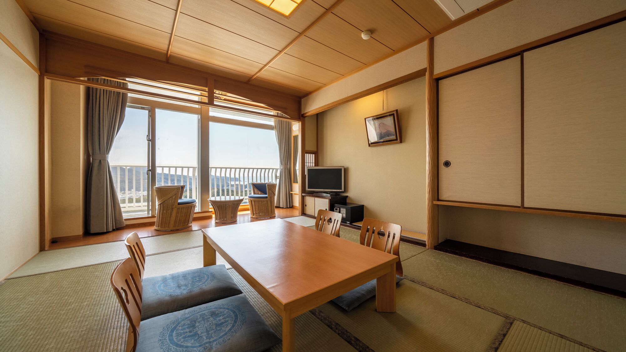 Une pièce de style japonais traditionnel, avec un sol recouvert de tatamis, une table en bois, des chaises, un téléviseur et une porte coulissante.