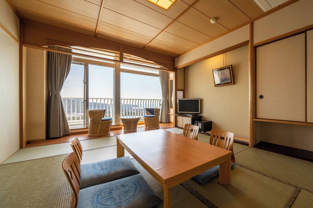A traditional Japanese room with tatami flooring, a wooden table, chairs, a television, and a sliding door.