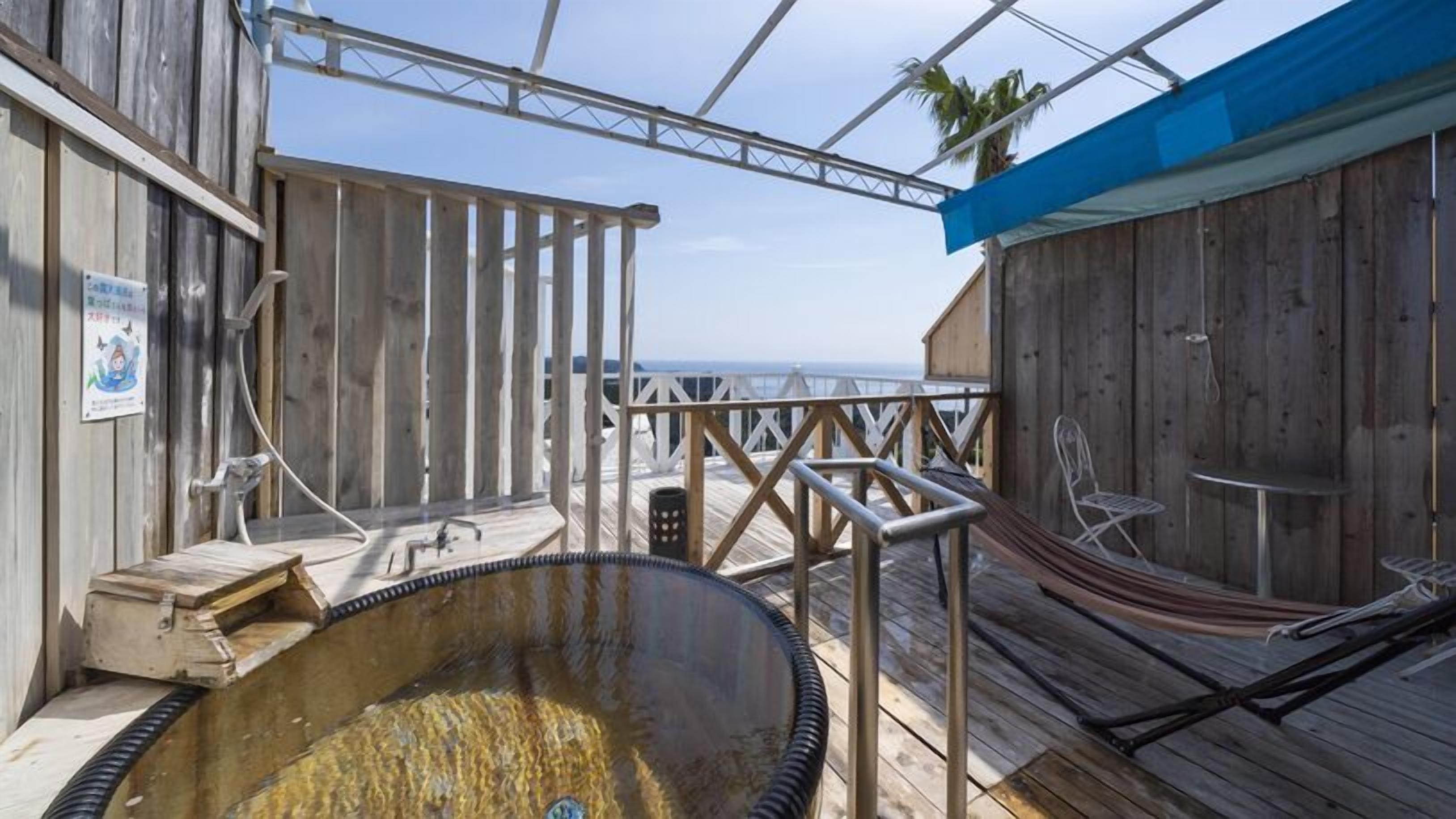 A wooden deck with a hot tub, a hammock, and a view of the ocean.