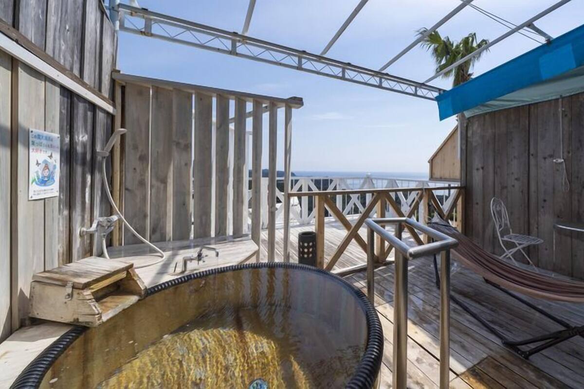 A wooden deck with a hot tub, a hammock, and a view of the ocean.