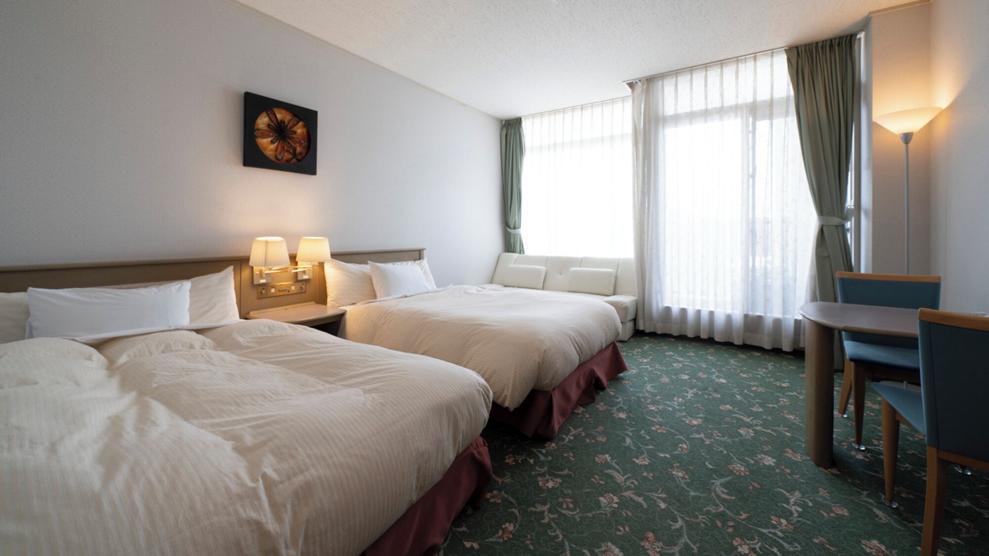 Une chambre d’hôtel avec deux lits, un bureau, une chaise, une lampe et une fenêtre avec des rideaux.