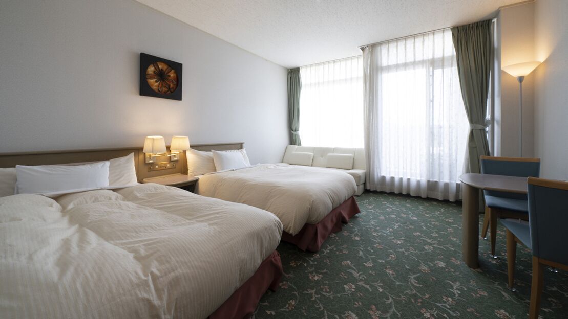 A hotel room with two beds, a desk, a chair, a lamp, and a window with curtains.