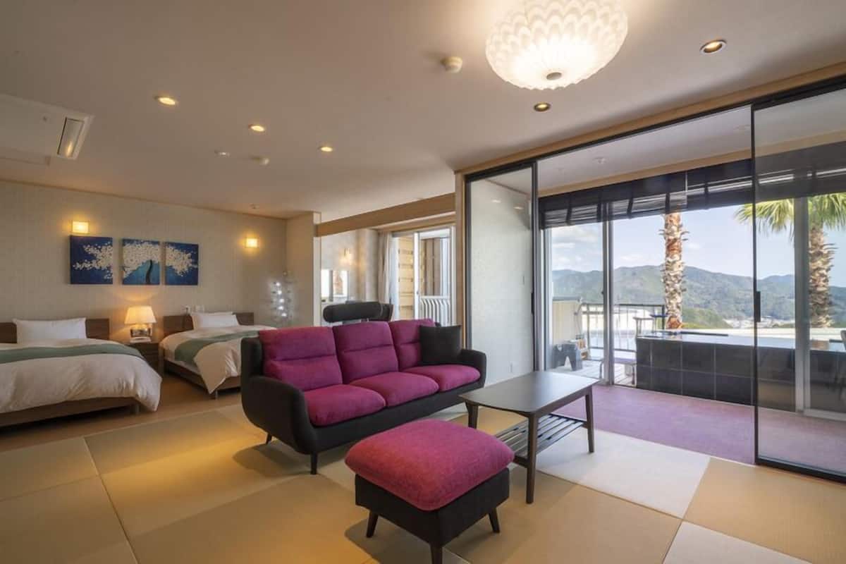 A modern hotel room with a bed, sofa, and a balcony with a view of the mountains.