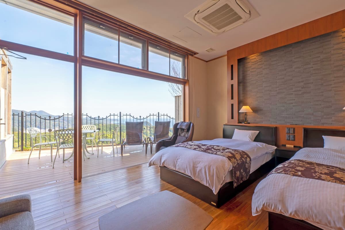 A bedroom with two beds, a balcony with chairs, and a view of the mountains.