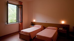 Une chambre avec deux lits, une fenêtre avec des rideaux, une table de chevet avec une lampe et un luminaire fixé au mur.