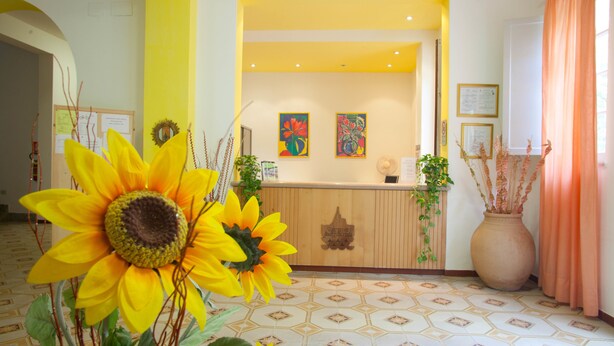 Un espace d’accueil avec un comptoir en bois, deux œuvres d’art encadrées et un grand vase contenant des plantes.