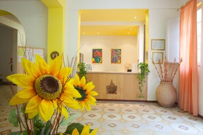 A reception area with a wooden counter, two framed artworks, and a large vase with plants. - Hotel Moderno (Acquappesa)