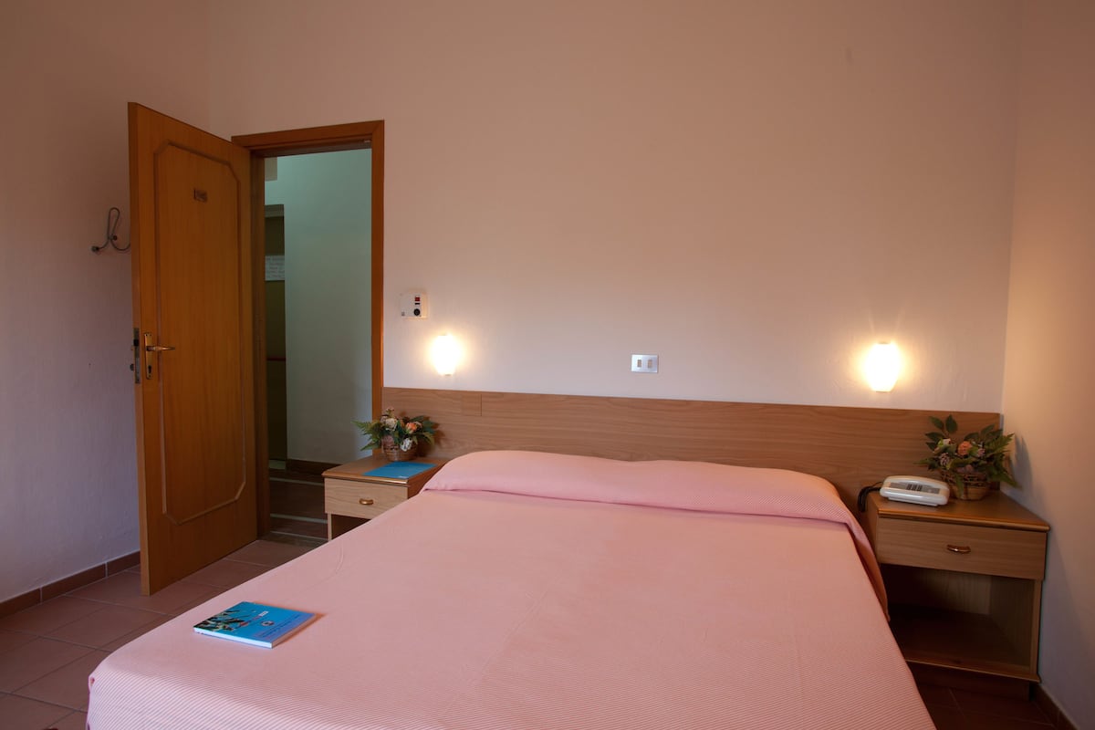 A hotel room with a bed, bedside table, nightstand, and an open door leading to a bathroom.