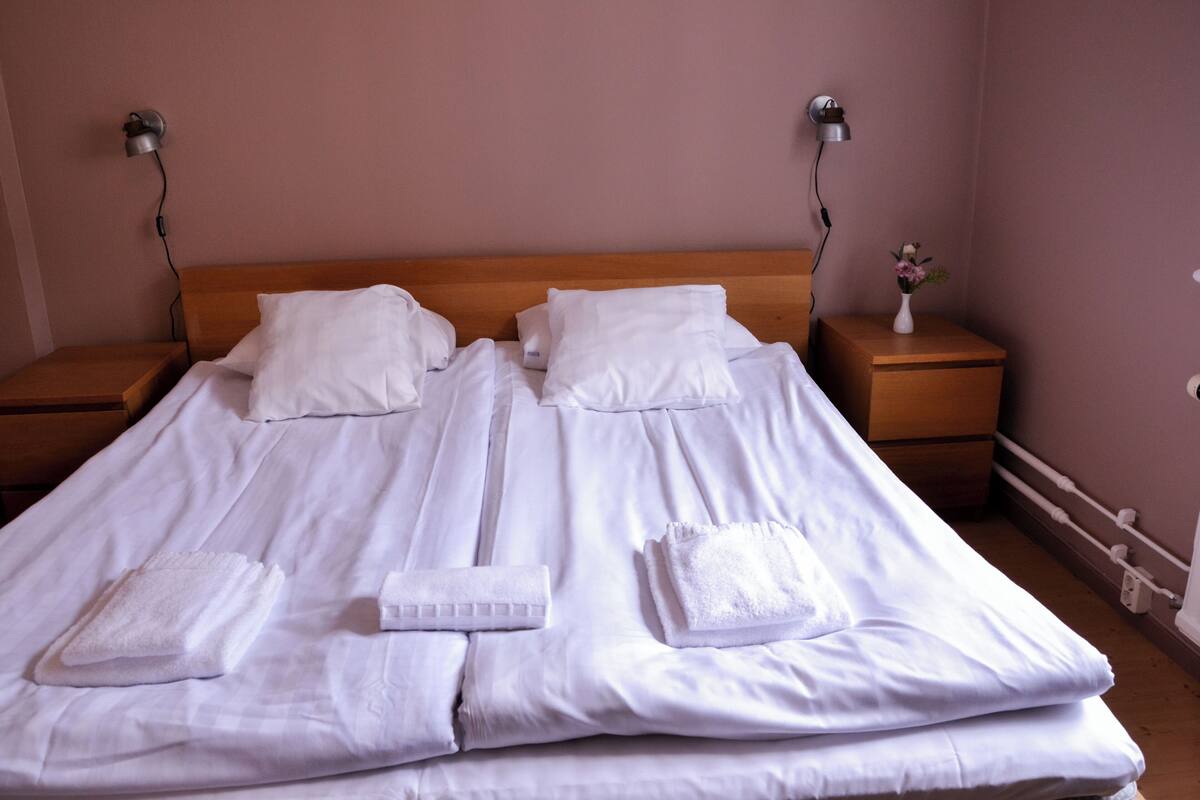 A neatly made bed with white linens, two bedside tables with lamps, and a small vase with flowers on one table.
