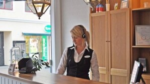 A reception desk with a wooden counter, a telephone, and a framed certificate on the wall. - Adelsgatan Bed & Breakfast (Visby)