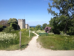 Ein unbefestigter Weg führt zu einer Steinschlossburg mit einer Bank und Wildblumen.