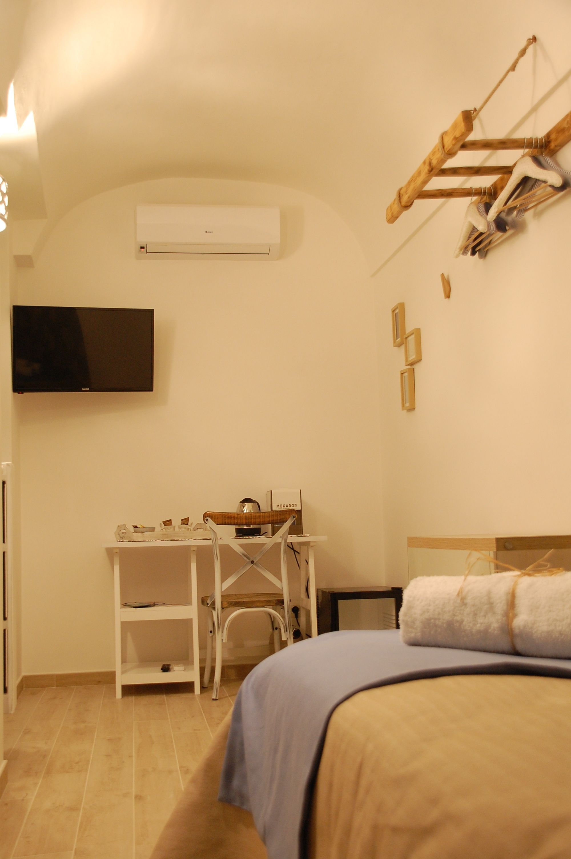 A bedroom with a bed, a desk with a chair, a television, and an air conditioning unit.