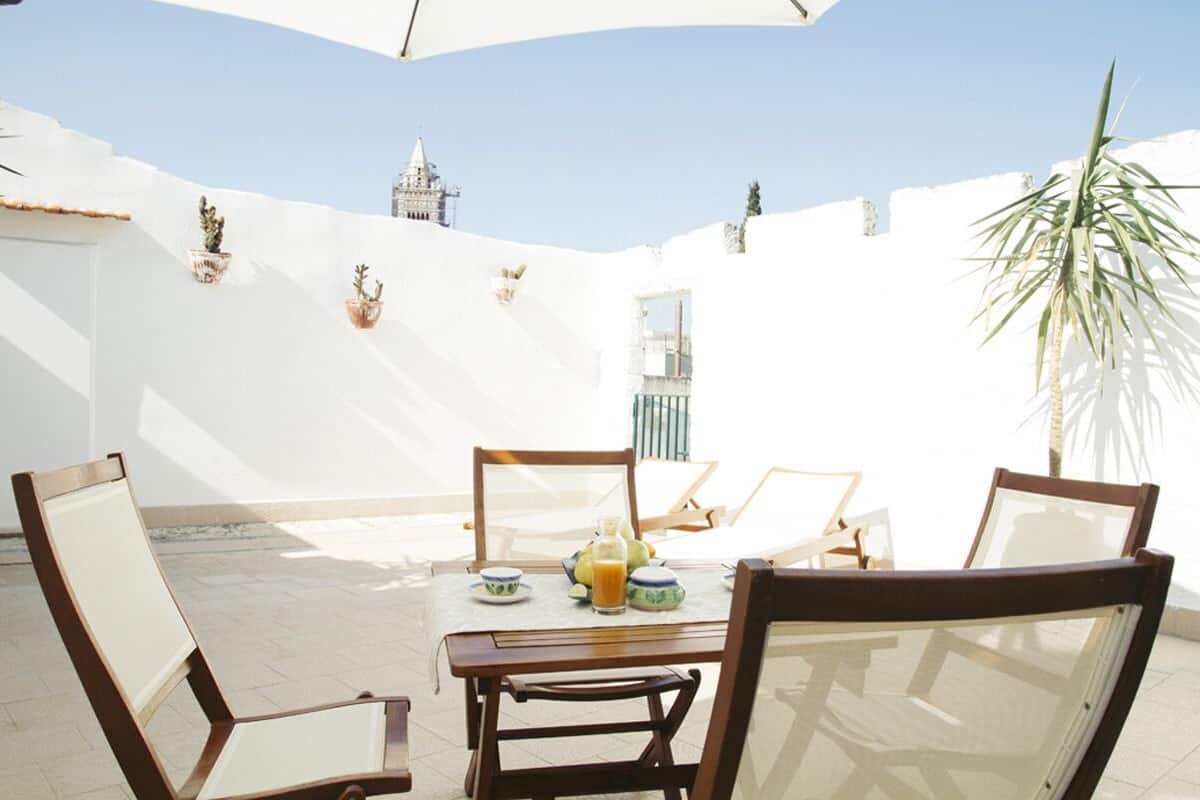 Un coin repas avec une table dressée pour quatre personnes, entourée de chaises, et un pot de fleurs placé à droite.