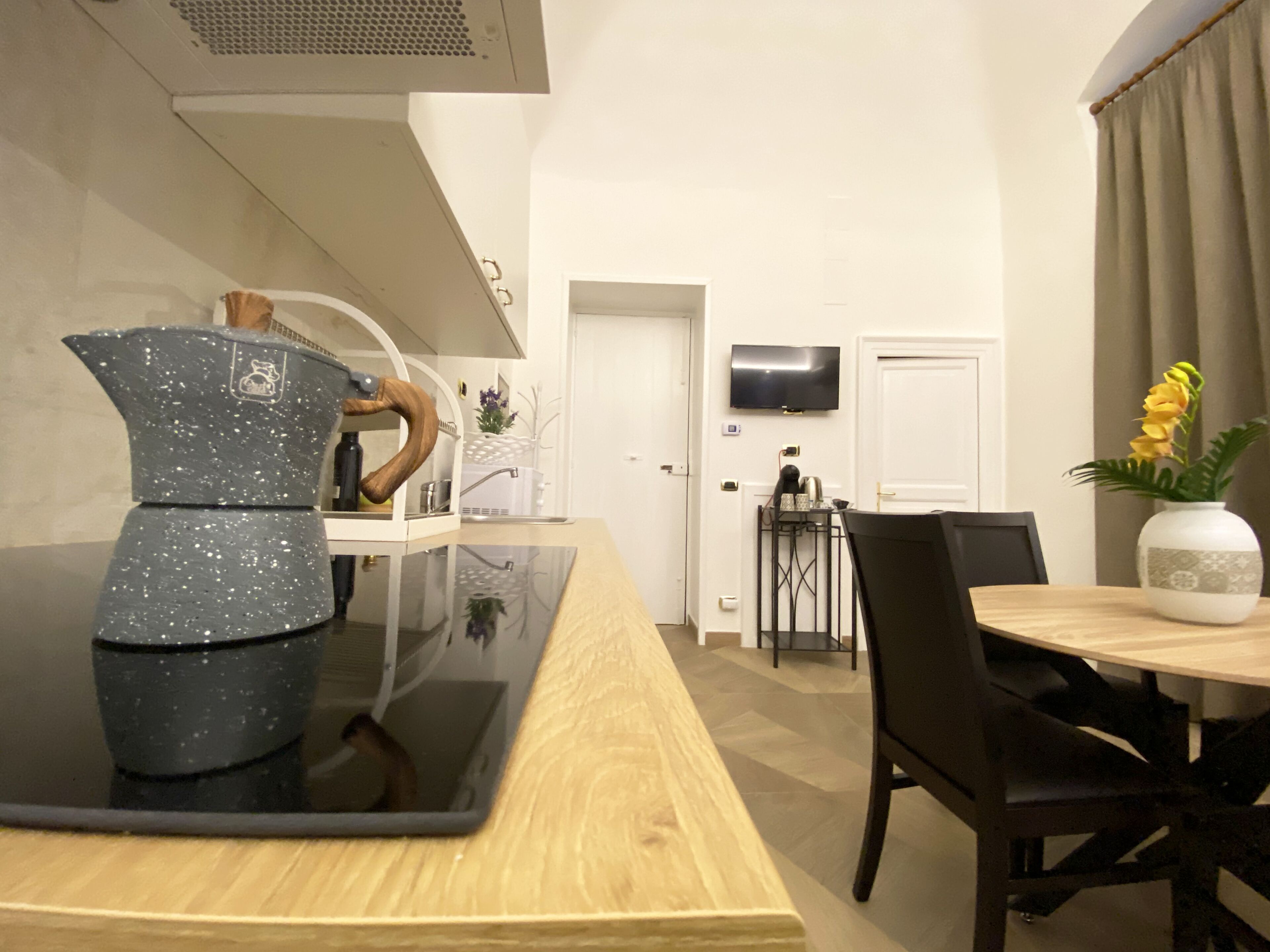 A modern kitchen with a black countertop, a wooden dining table, and a vase with flowers.