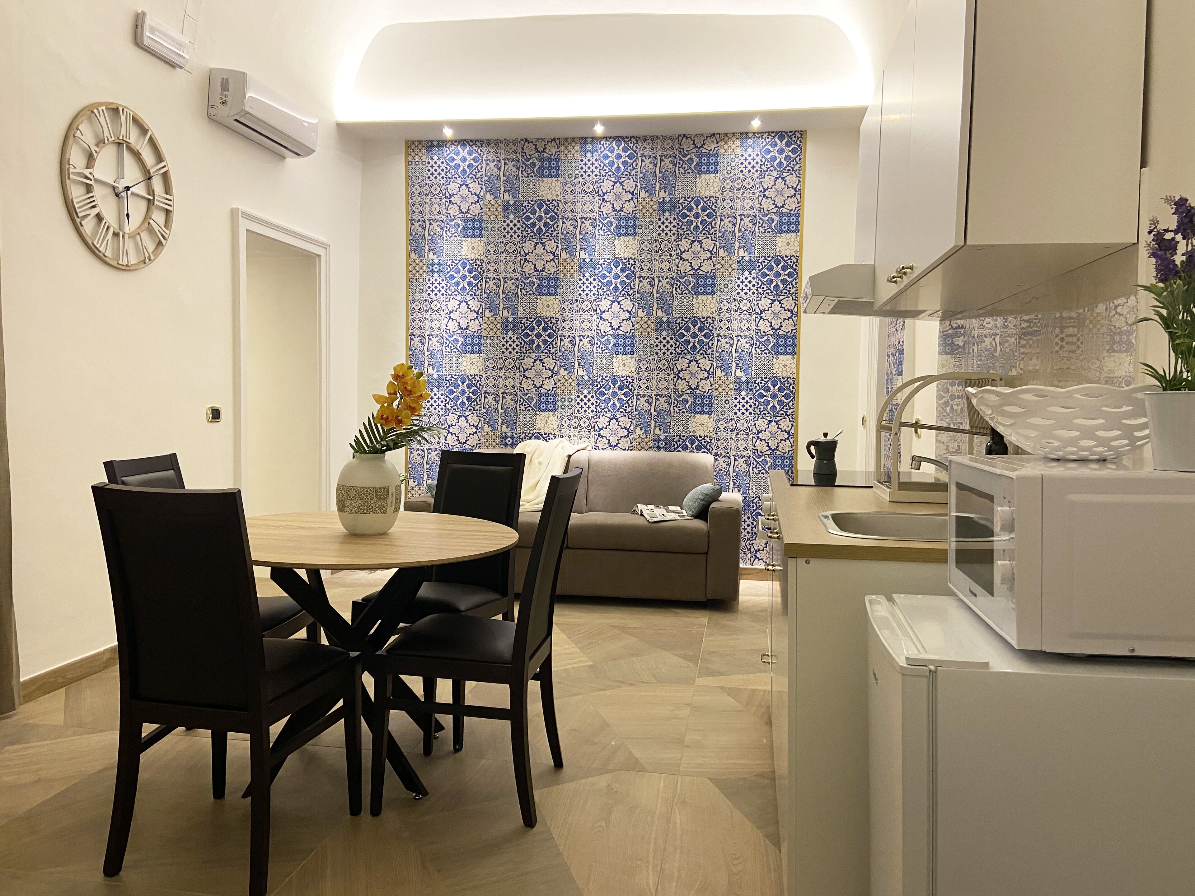 A modern kitchen with a dining area, featuring a clock, a patterned backsplash, and a microwave.