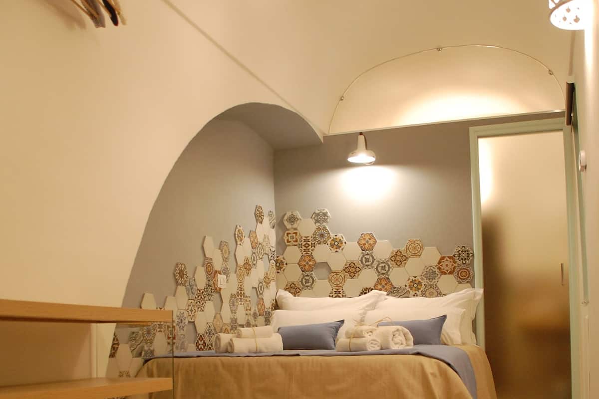 Une chambre à coucher avec un lit, un banc en bois, un mur décoratif et un luminaire suspendu.