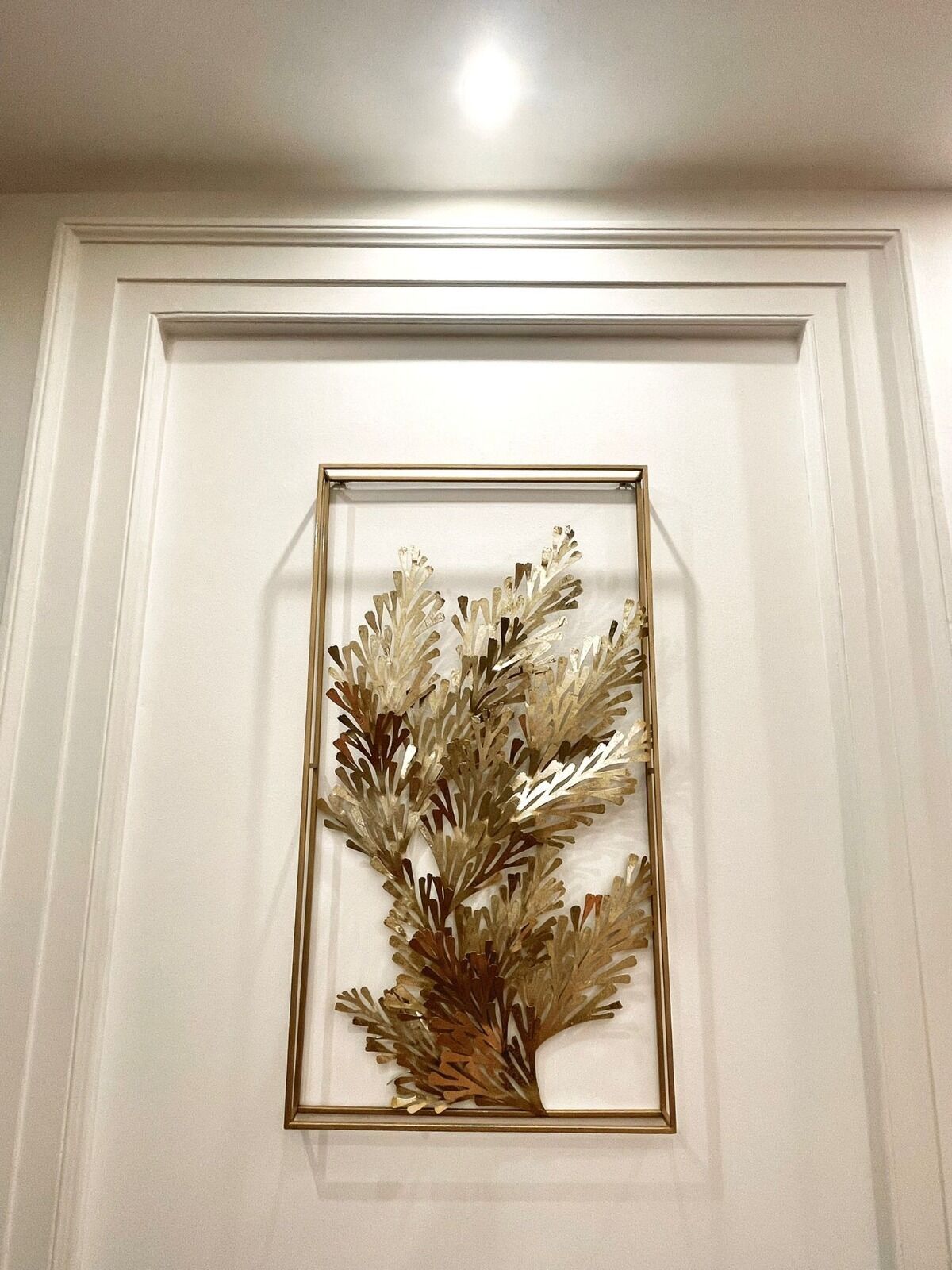 A framed decorative piece with a leaf-like design on a wall.