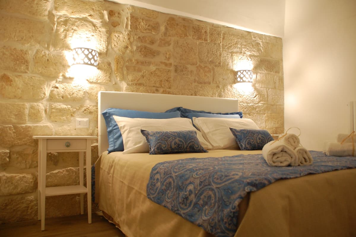 Un lit avec une tête de lit, une table de chevet et un mur à la texture pierre.