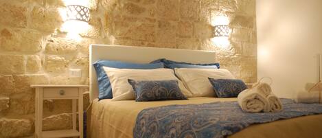 A bed with a headboard, a bedside table, and a wall with stone texture.