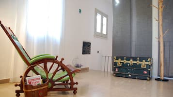 Una stanza con una sedia a dondolo in legno, una poltrona imbottita verde, un secchio di legno con un cartello e una valigia vintage.