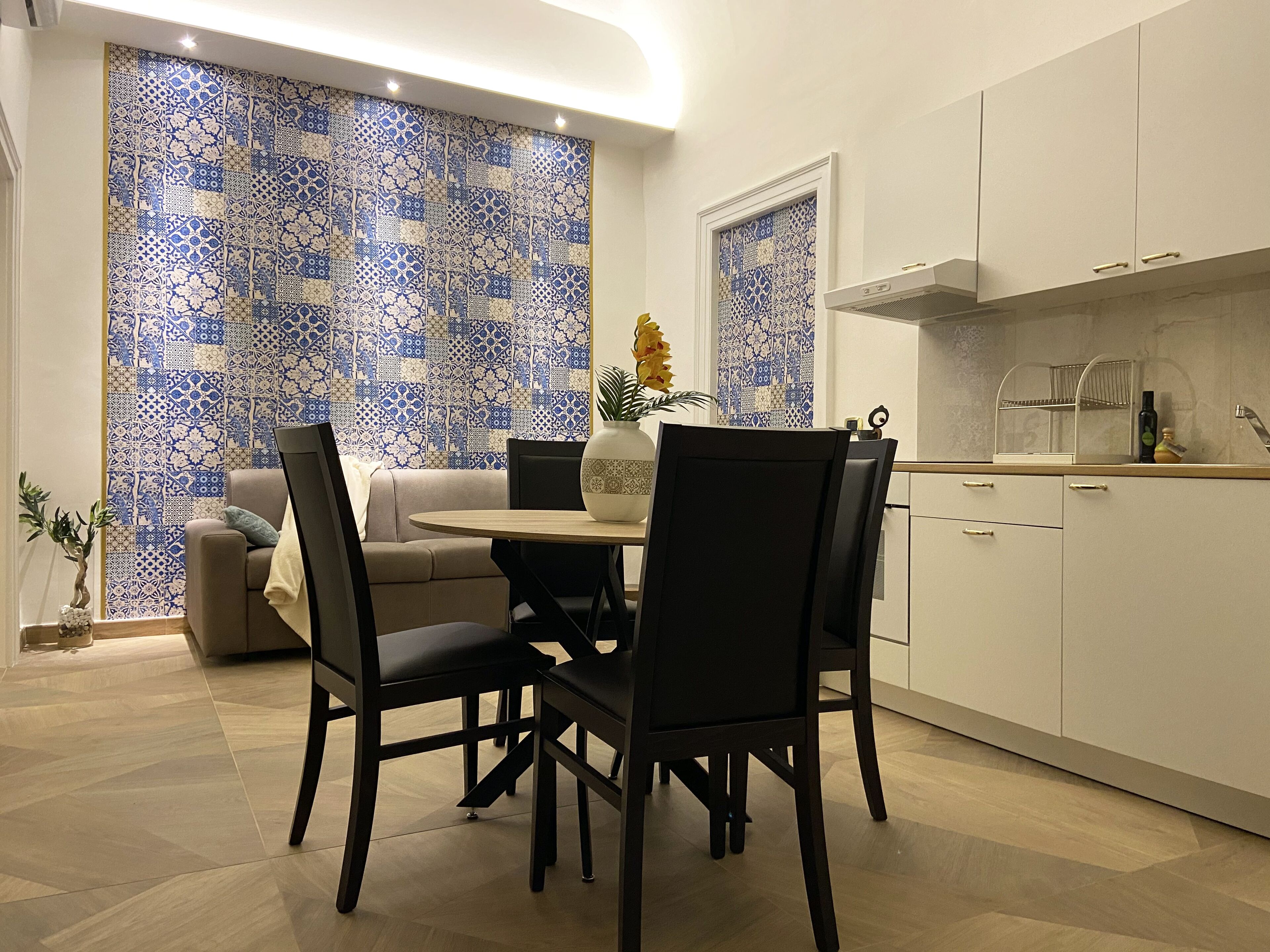 Una cocina moderna con armarios blancos, un comedor con una mesa redonda y sillas, y un salpicadero de azulejos azul y blanco con diseño.