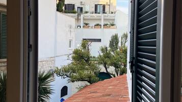 Vista desde un balcón con techo de tejas rojas, que da a una calle con edificios y árboles.