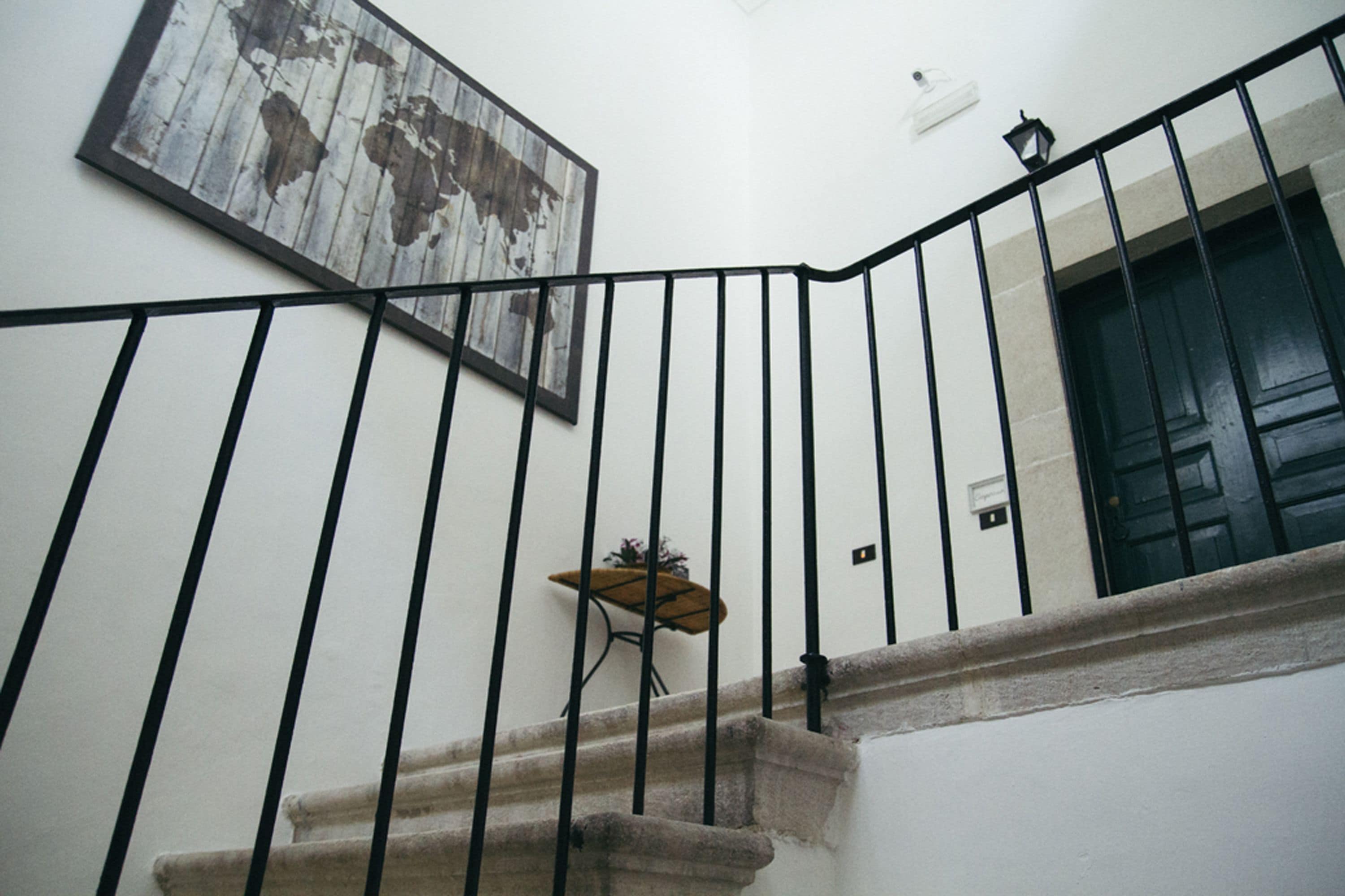 Un escalier avec une rampe en métal noir, une carte du monde accrochée au mur et une porte dotée d’une fenêtre.