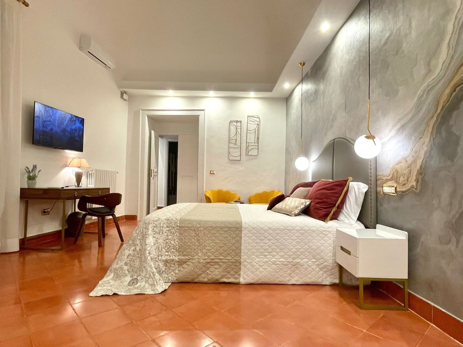 A bedroom with a bed, a desk, a chair, a TV, and a wall with a light fixture.
