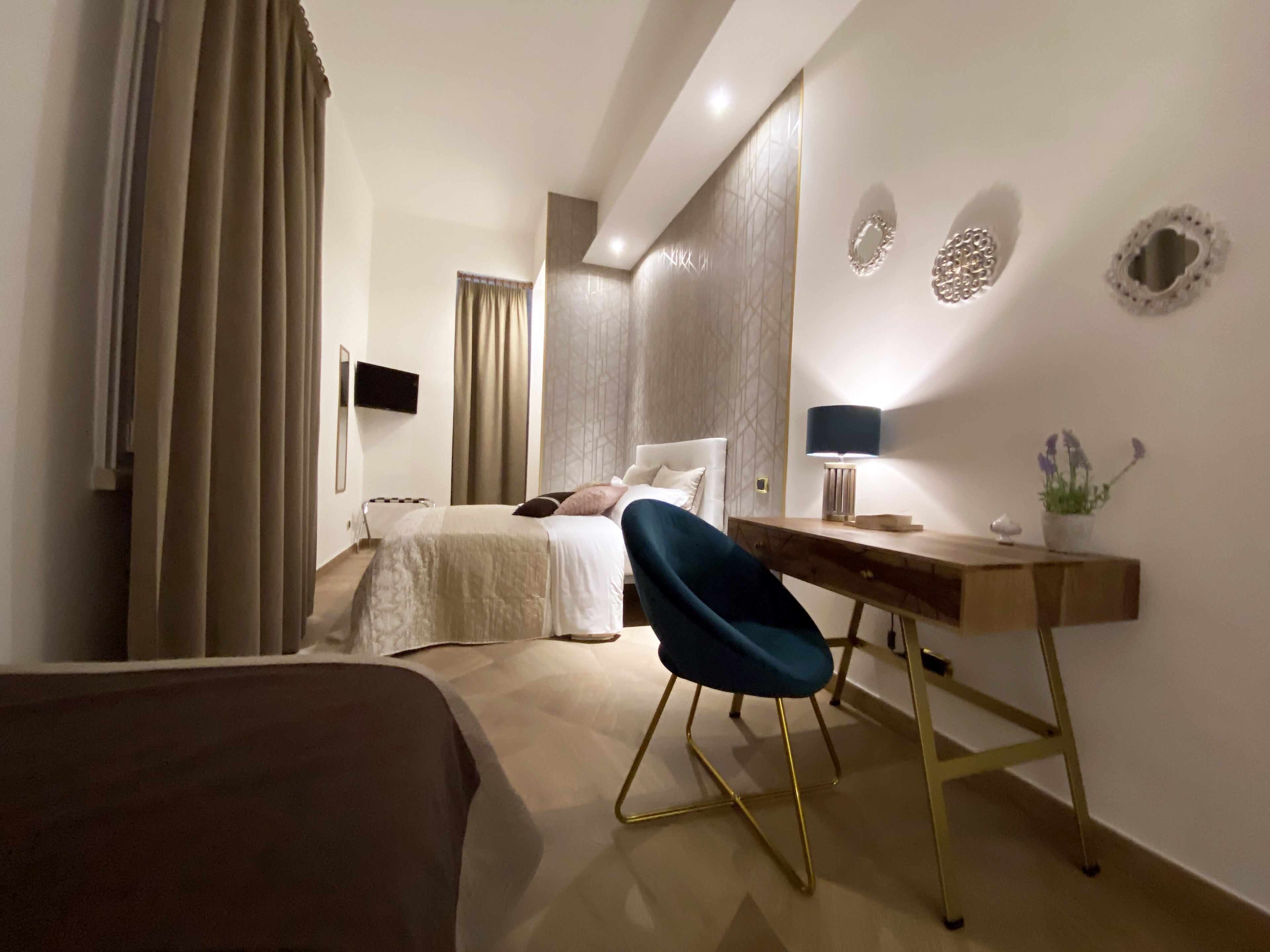 A modern hotel room with a bed, a desk, a chair, a TV, and decorative wall art.