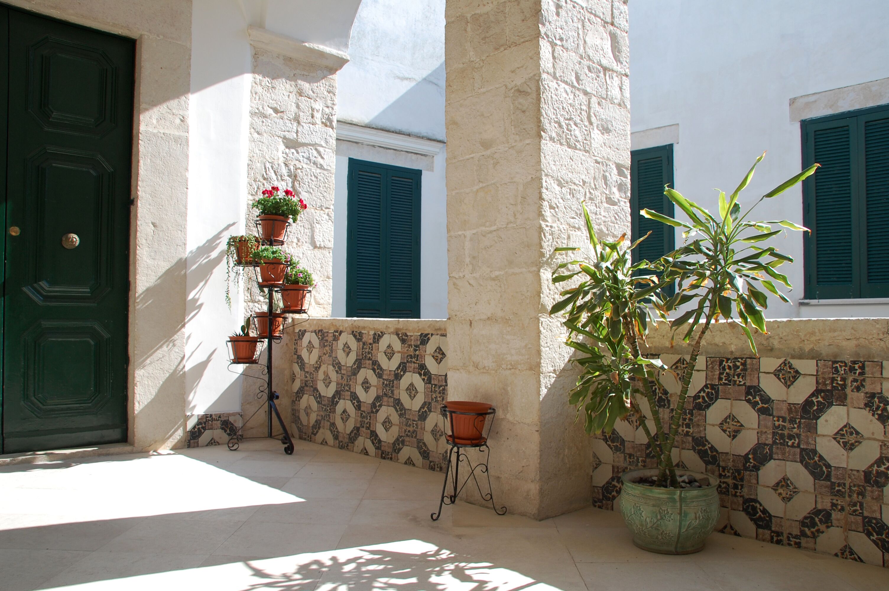 A courtyard with a green door, tiled walls, and potted plants.