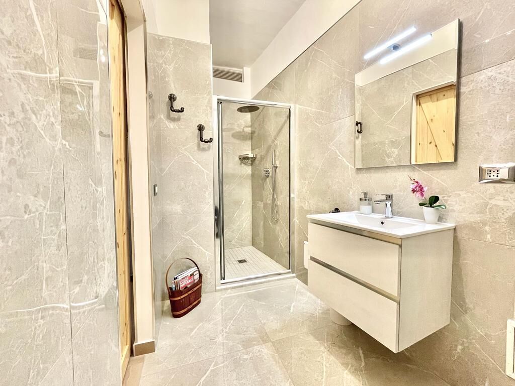 A modern bathroom with a glass shower enclosure, a white vanity with a mirror, and marble flooring.
