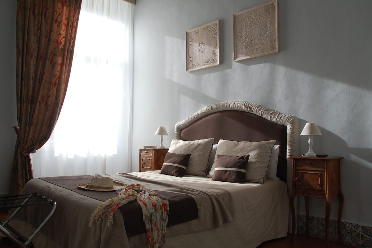 Une chambre à coucher bien rangée, avec un grand lit, deux tables de chevet, une chaise et une fenêtre avec des rideaux.