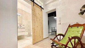 Een kamer met een schuifdeur naar een badkamer, een houten schommelstoel en een eethoek met stoelen.