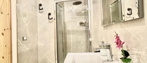 Un baño moderno con cabina de ducha de vidrio, un lavamanos blanco con espejo arriba y una pequeña planta en maceta sobre la encimera.