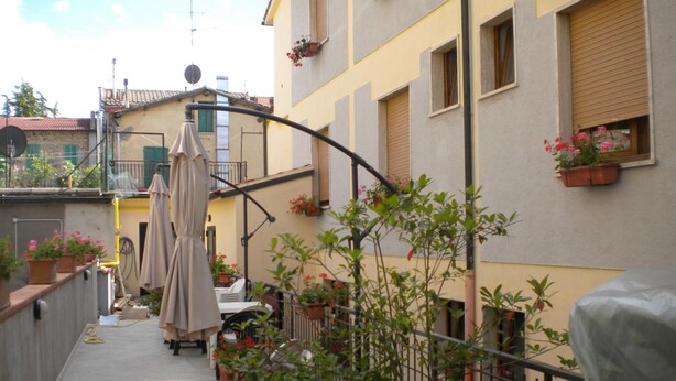 A narrow outdoor corridor with potted plants, a covered seating area, and a building with balconies and flower boxes. - Albergo Ristorante La Bocca di Bacco (Abbadia San Salvatore)