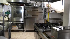 A commercial kitchen with stainless steel appliances, including ovens, a stove, and hanging pots. - Albergo Ristorante La Bocca di Bacco (Abbadia San Salvatore)