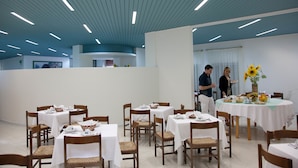 Een eetgedeelte met gedekte tafels, houten stoelen en een plafond met lineaire verlichting.