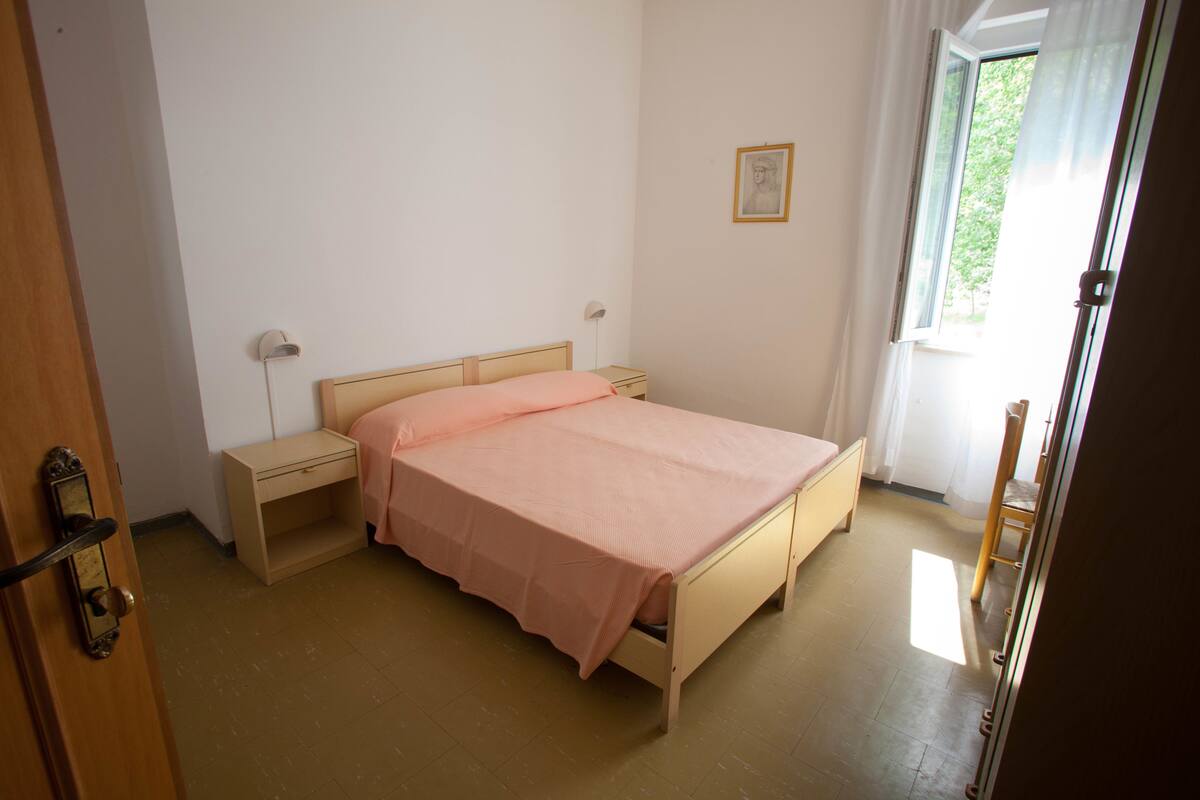 Une chambre avec un lit simple, une table de chevet, une commode et une fenêtre avec des rideaux.