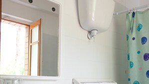Een badkamer met een wit wastafel, een rode kraan en een wit toilet. Er hangt een spiegel boven de wastafel en een douchegordijn met stippen.