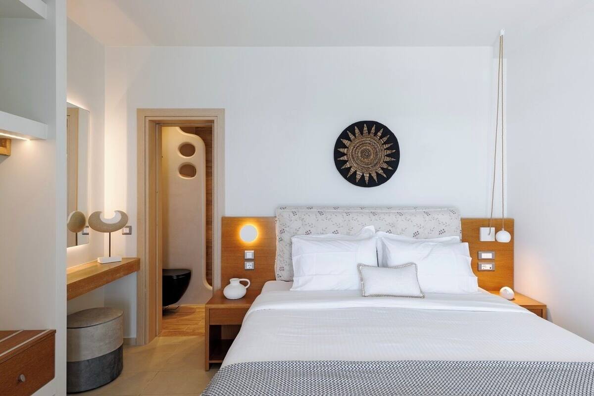 Habitación de hotel moderna con una cama grande, mesitas de noche con lámparas, un adorno en la pared y una puerta que conduce a un baño.