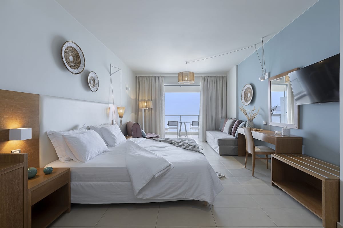 Una habitación de hotel moderna con una cama grande, un escritorio, un televisor y un balcón con vistas.