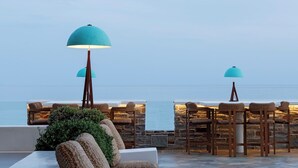An outdoor seating area with a stone wall backdrop, a white sofa, and a bar area with stools and a table.