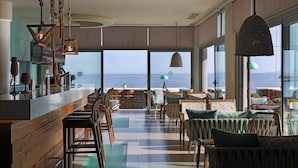 A modern bar area with a view of the sea, wooden furniture, and hanging pendant lights.