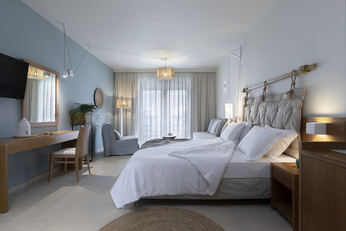 Un dormitorio moderno con una cama grande, un escritorio y una silla. Hay un televisor en la pared y una ventana con cortinas.
